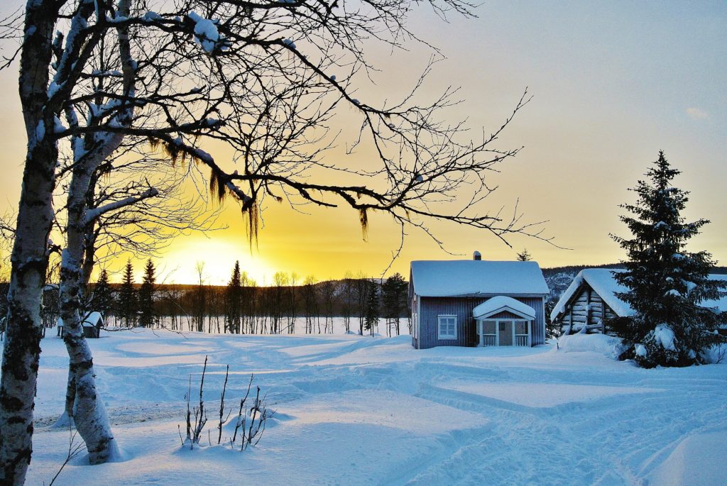 r: Snötäckt gård i norrländskt vinterlandskap med björkar och skymningsljus.