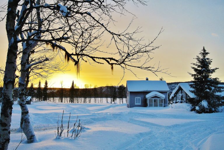 r: Snötäckt gård i norrländskt vinterlandskap med björkar och skymningsljus.