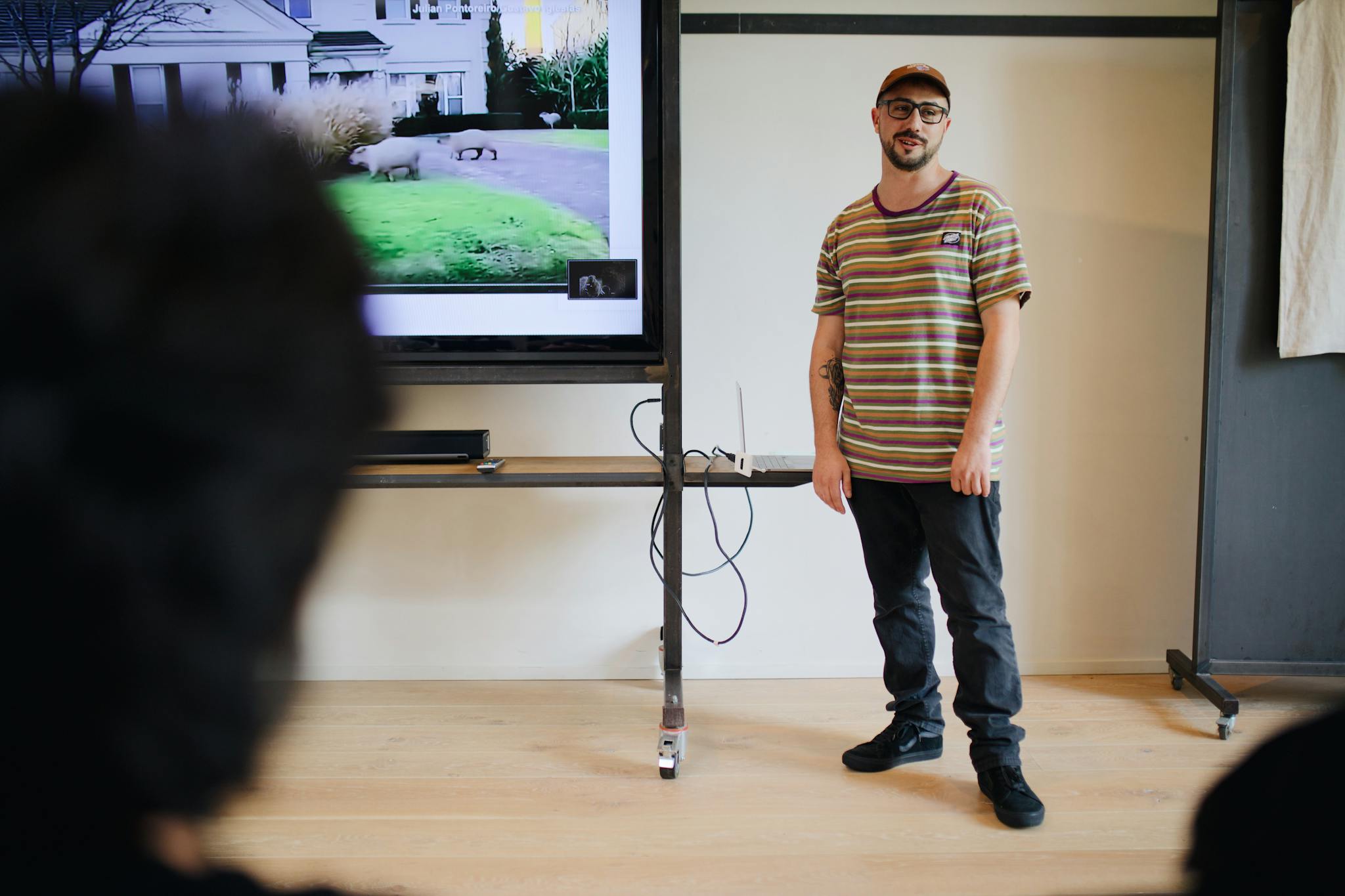 A man giving a casual presentation in a modern classroom with a large screen display.